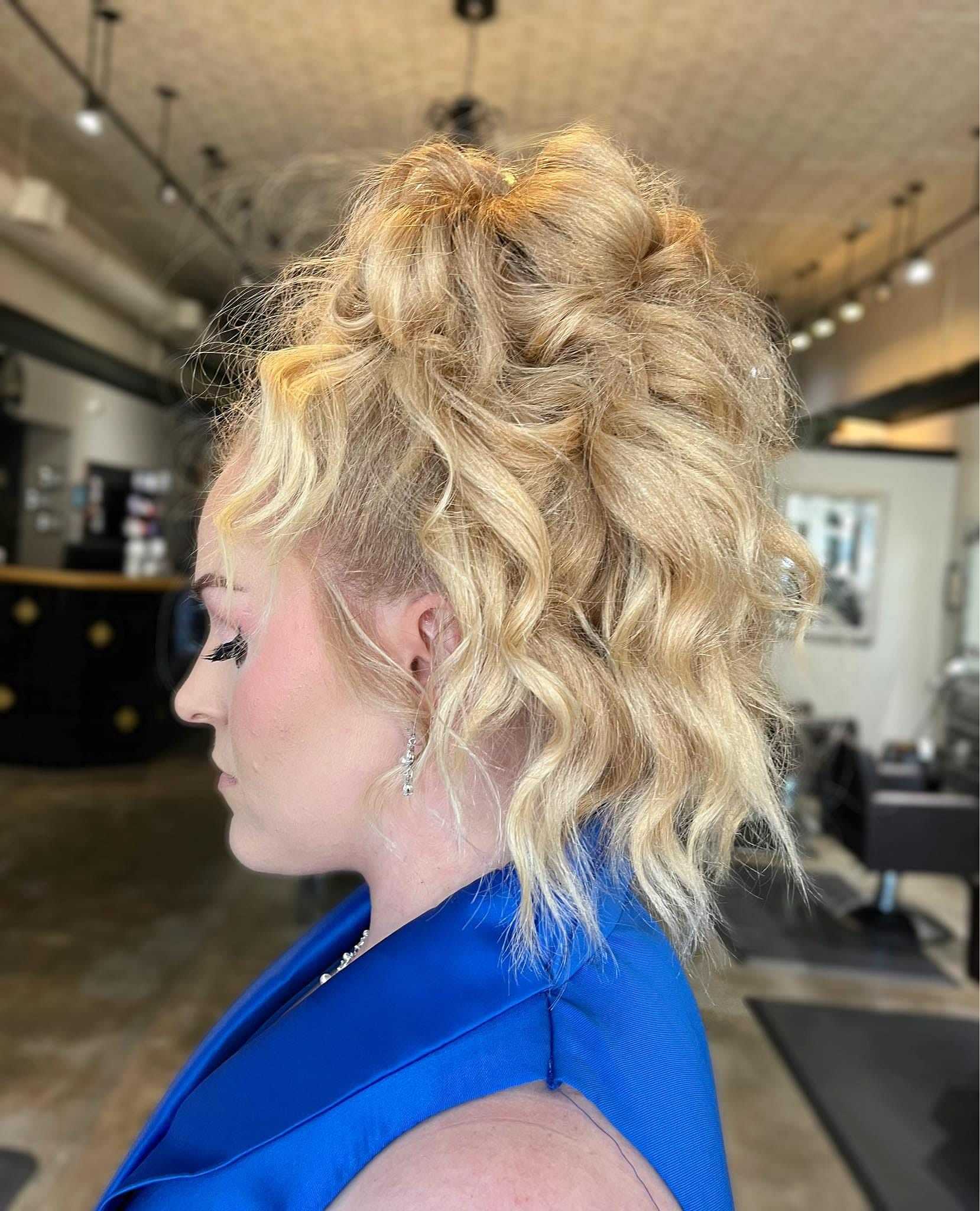 Woman with styled wavy blonde hair in a salon, wearing a blue outfit, side profile.