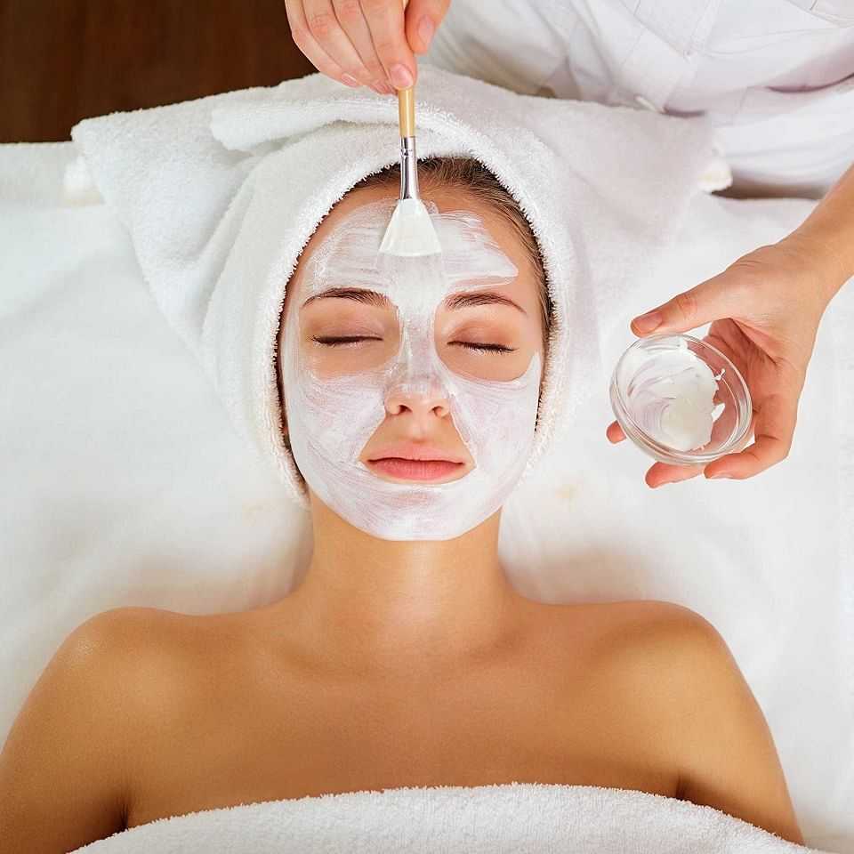 Person receiving a facial treatment with a white mask applied by a beautician at a spa.