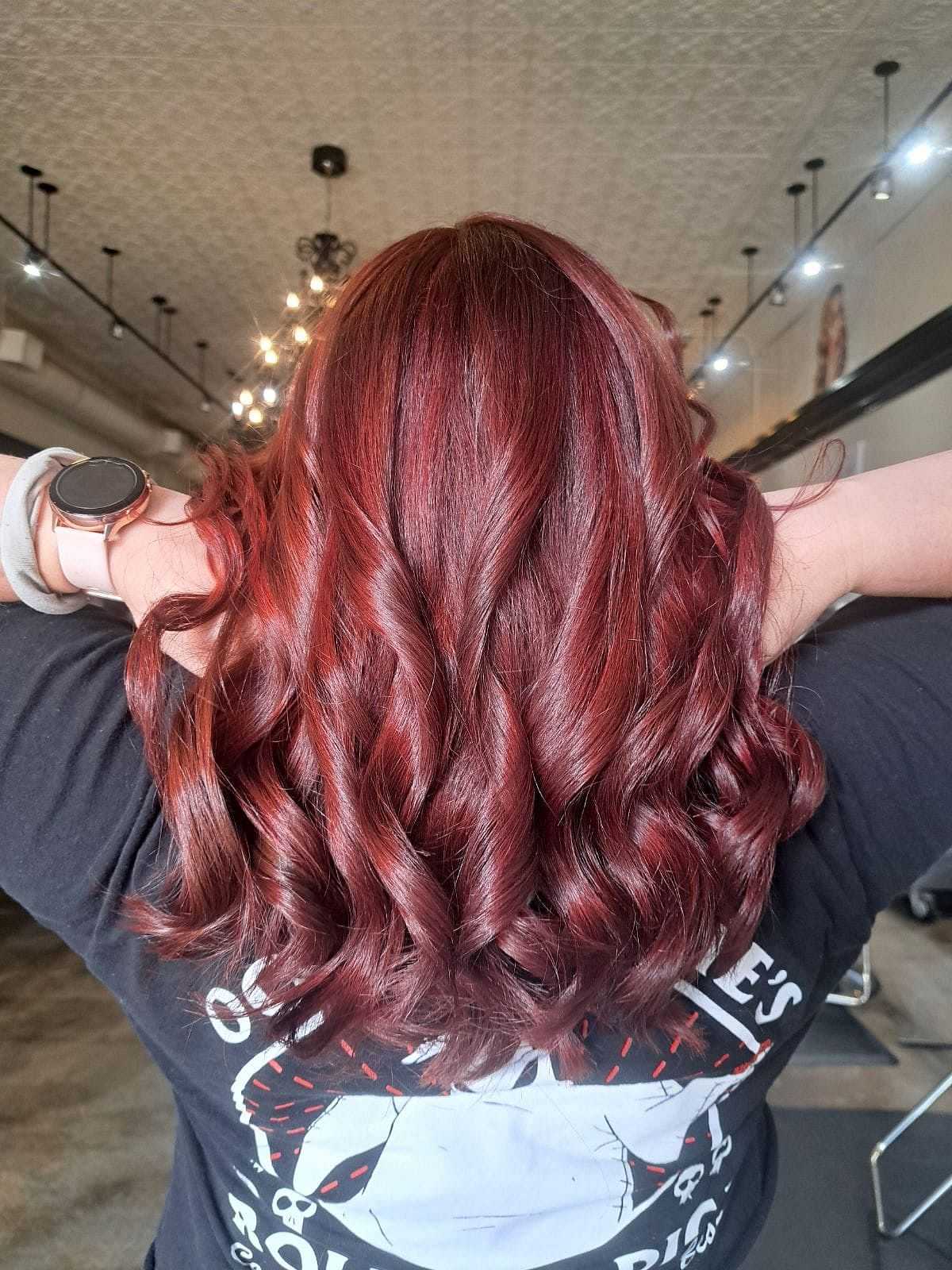 Woman with vibrant red curly hair facing away in a stylish salon with a modern interior.