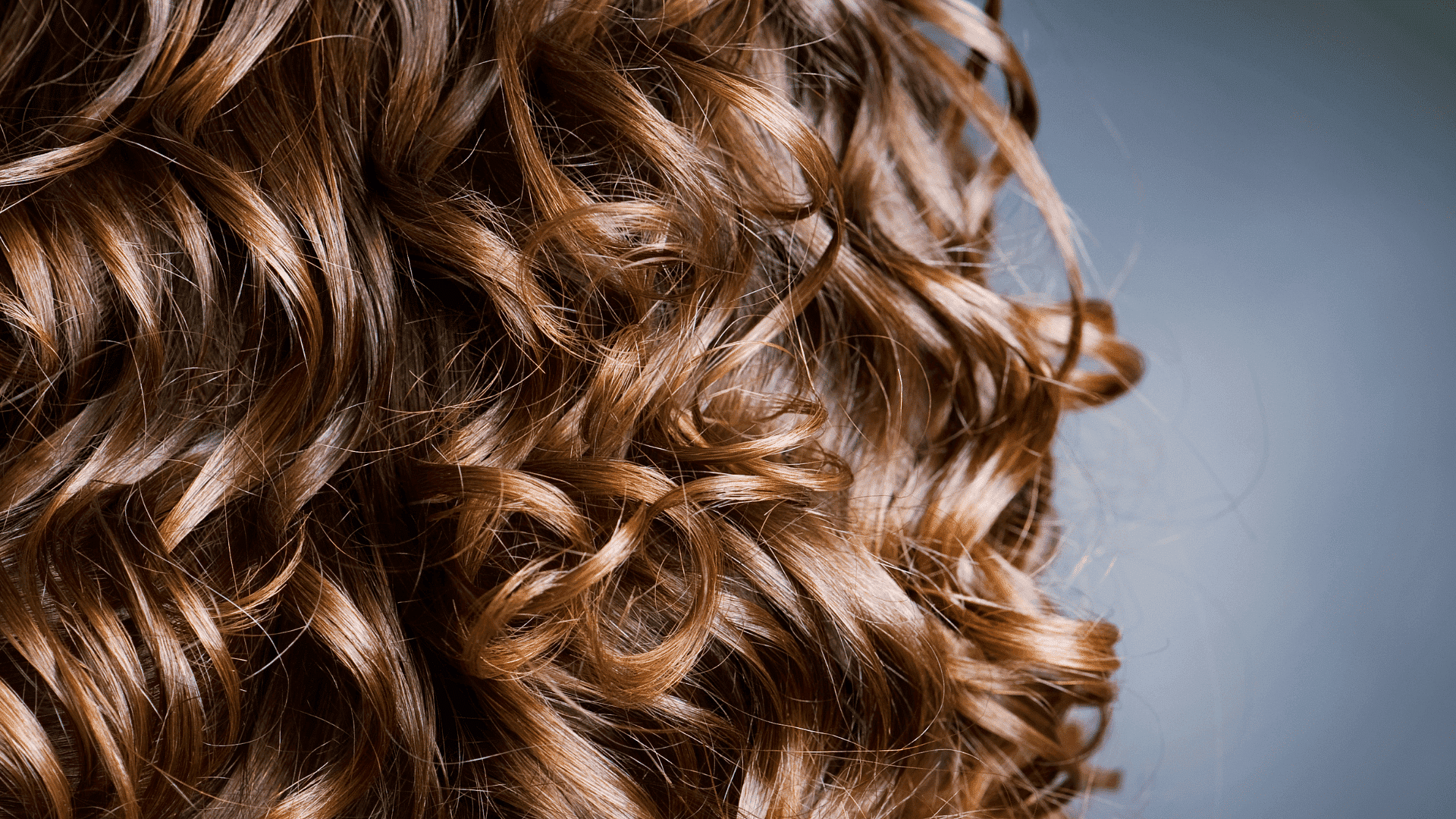 Close-up of wavy brown hair against a soft blue-gray background.